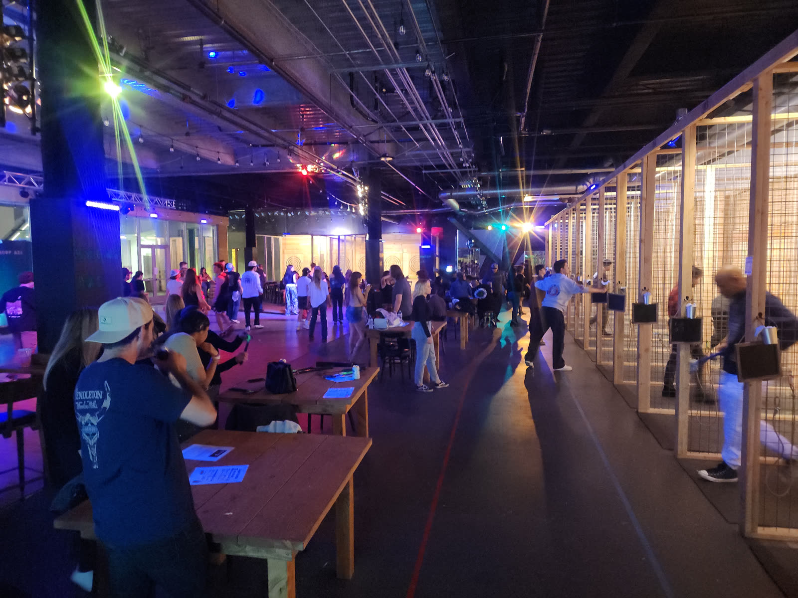 Crowded Whoop Axe venue with guests throwing axes in lanes and a full dance floor under stage lighting