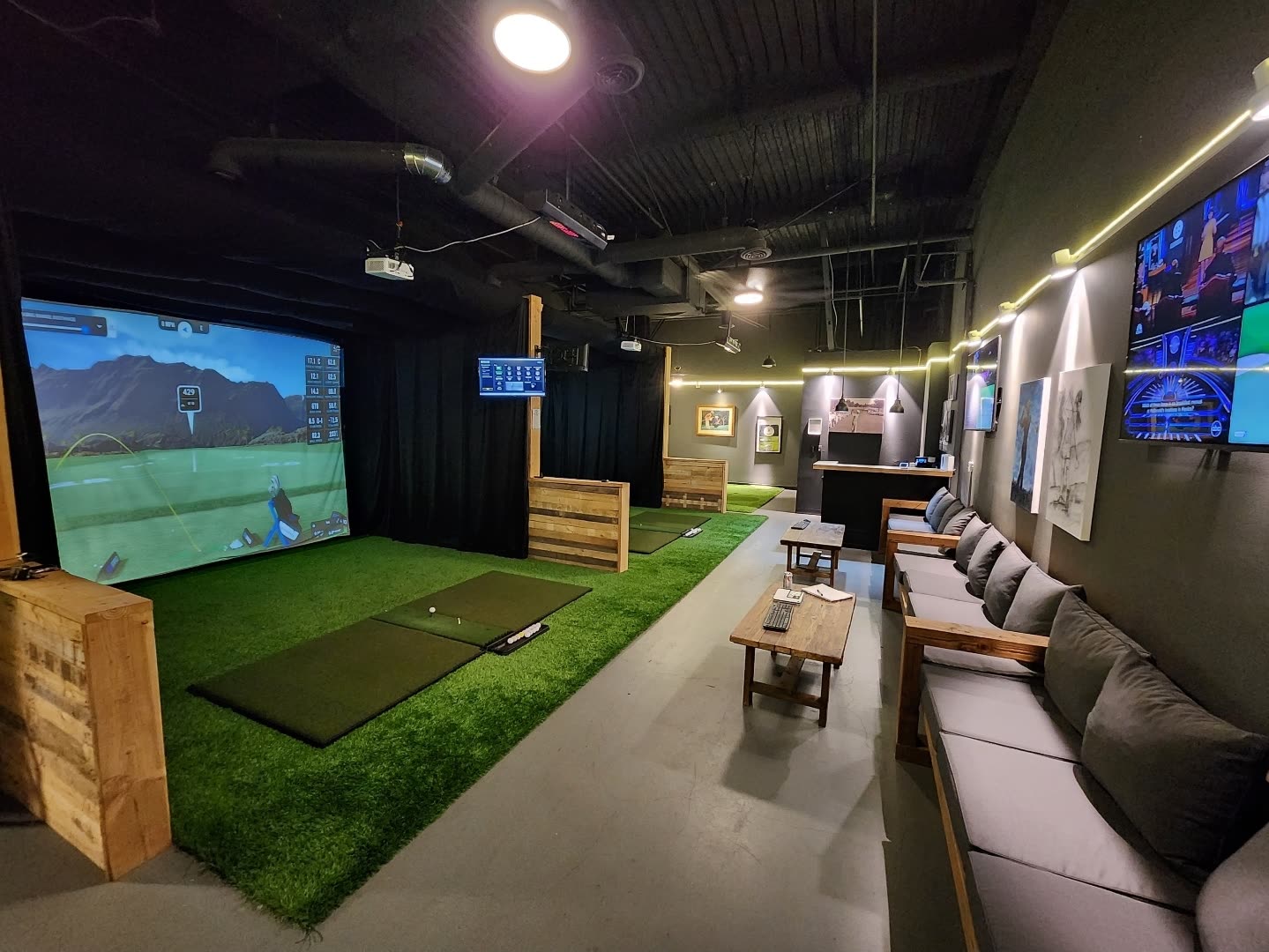 Golf simulator room with two hitting bays, sofas and wall-mounted televisions